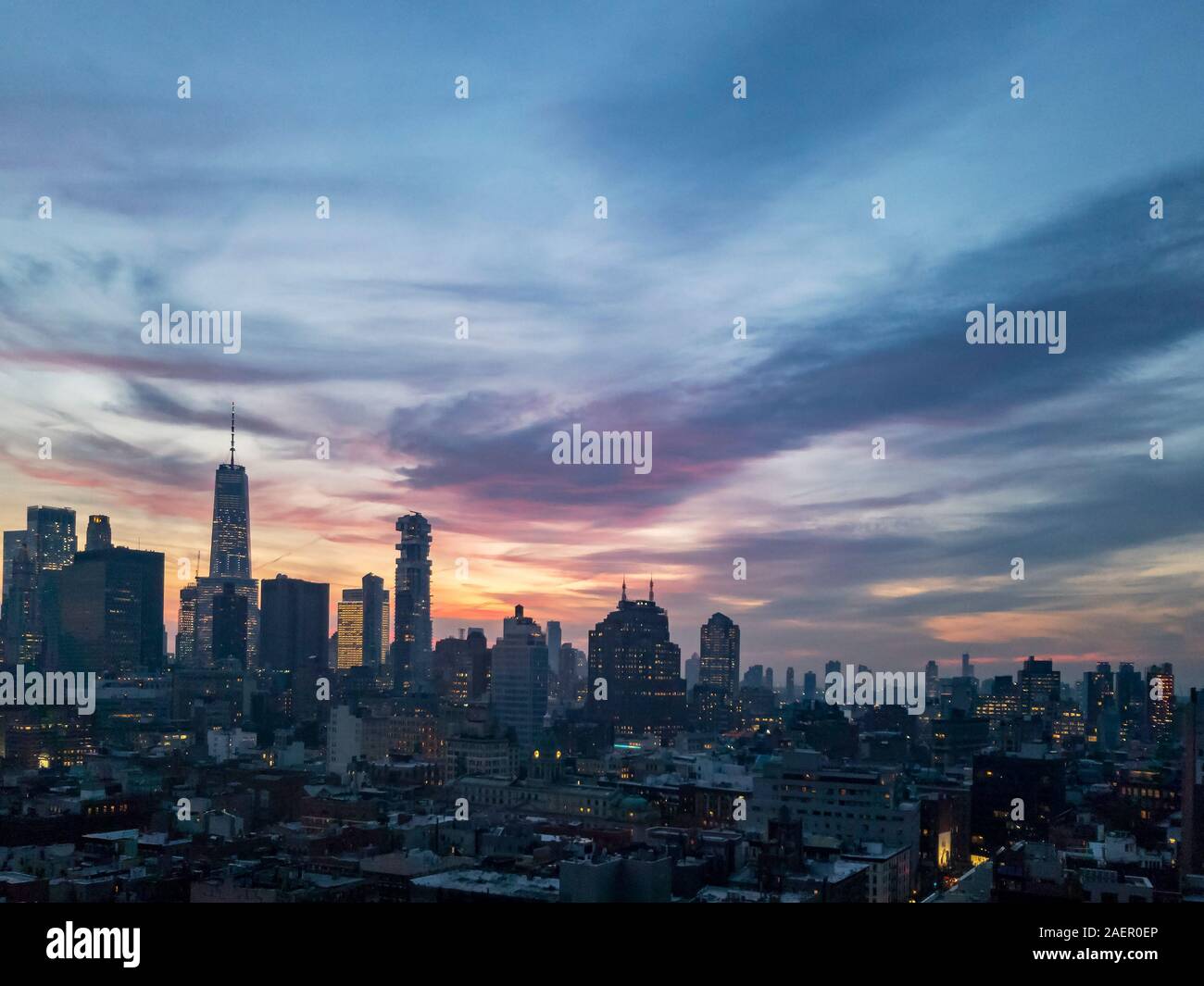 Dusk falls over the downtown Manhattan skyline with the lights of the skyscrapers contrasted against the colorful evening sunset sky in New York City Stock Photo