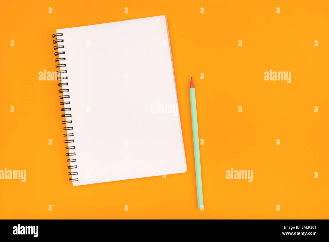 Empty notebook and pencil on orange background, top view. Stock Photo