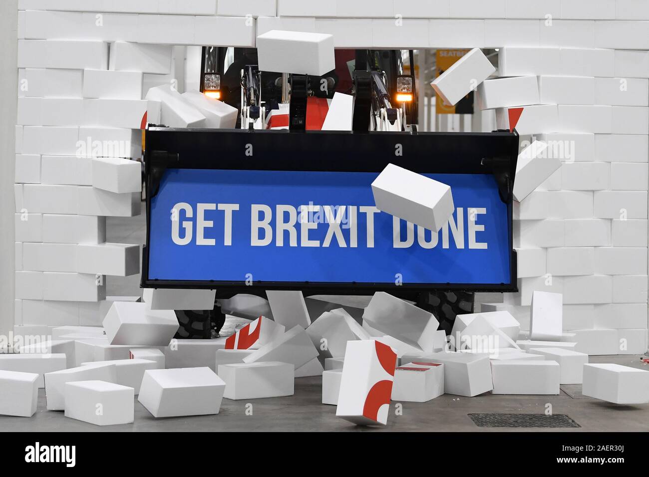 Prime Minister Boris Johnson drives a Union flag-themed JCB, with the words 'Get Brexit Done' inside the digger bucket, through a fake wall emblazoned with the word 'Gridlock', during a visit to JCB cab manufacturing centre in Uttoxeter, while on the General Election campaign trail. Stock Photo