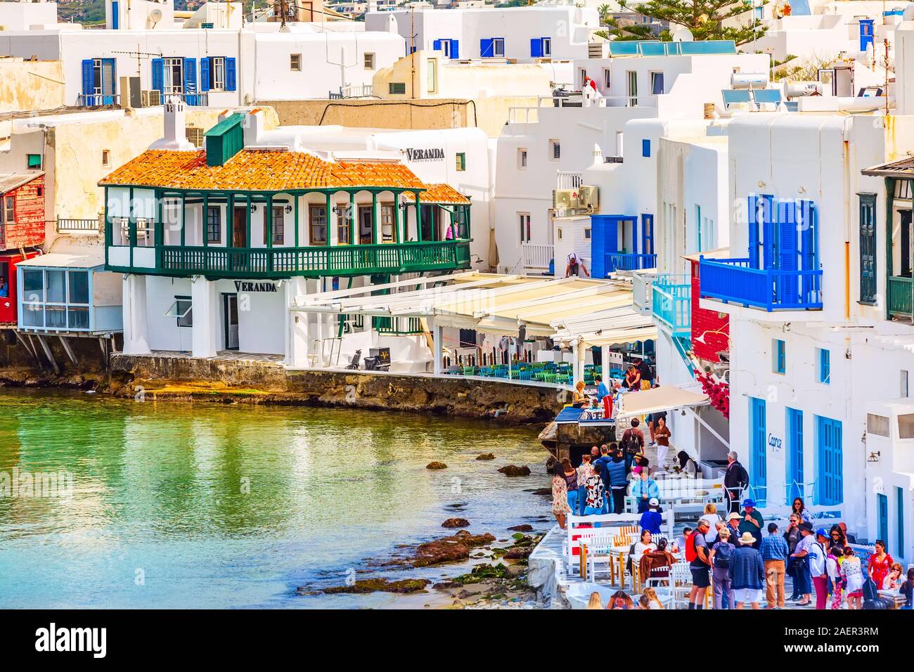 Mykonos, Greece - April 23, 2019: People, promenade with chairs and tables in typical greek tavern in Little Venice part of Mikonos town Stock Photo