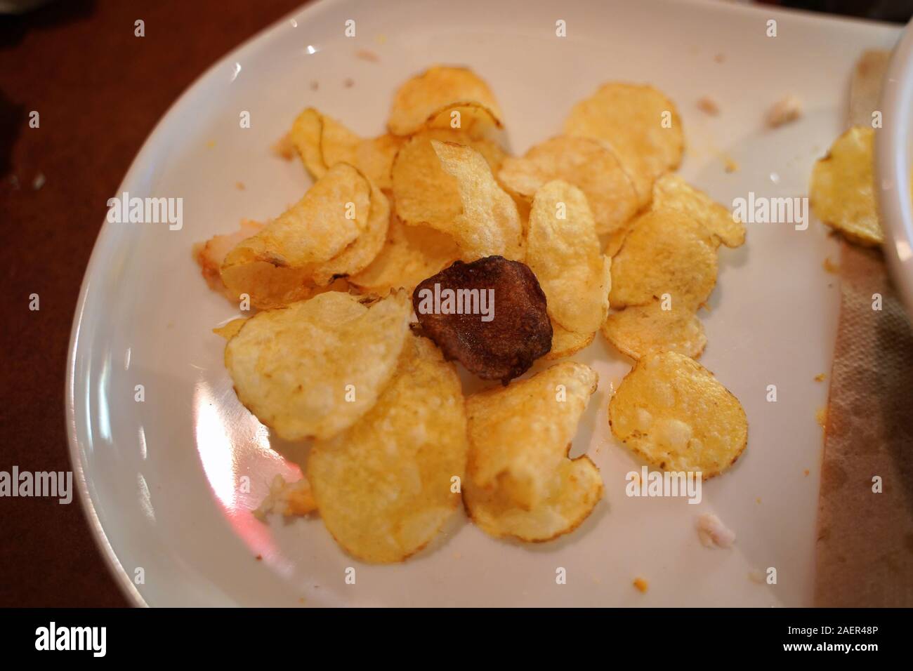 A lone burnt oily potato chip sticking out among the properly fried ones on a plate. Stock Photo