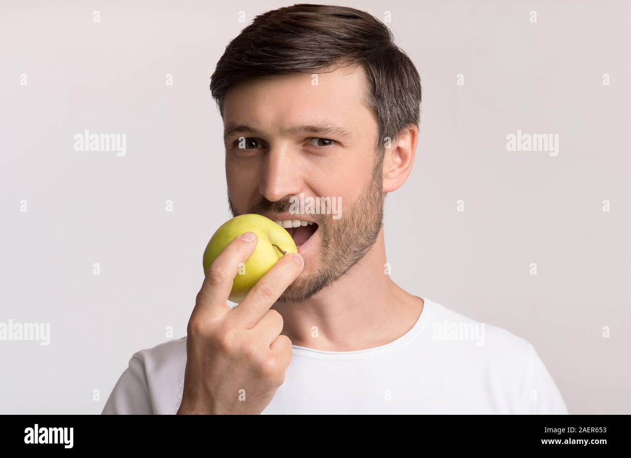 Happy Man Biting Apple Standing Over White Studio Background Stock Photo