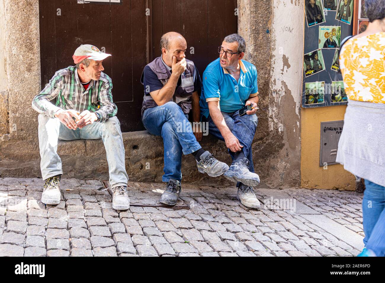 Three Portuguese  workmen spend their lunch hour sitting on a doorstep watching pedestrians pass by Stock Photo