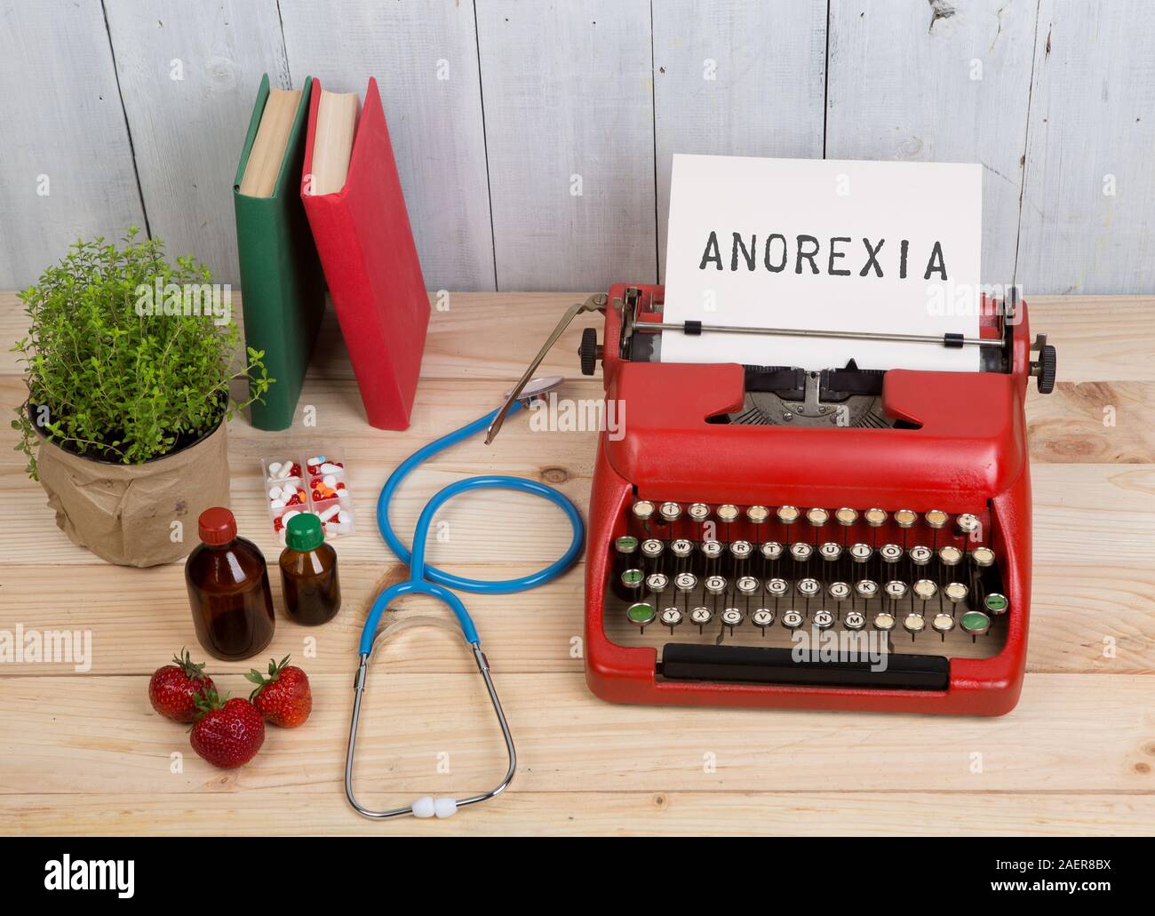 Eating disorder concept - typewriter with text Anorexia, blue stethoscope, pills, red typewriter, strawberries on wooden table Stock Photo