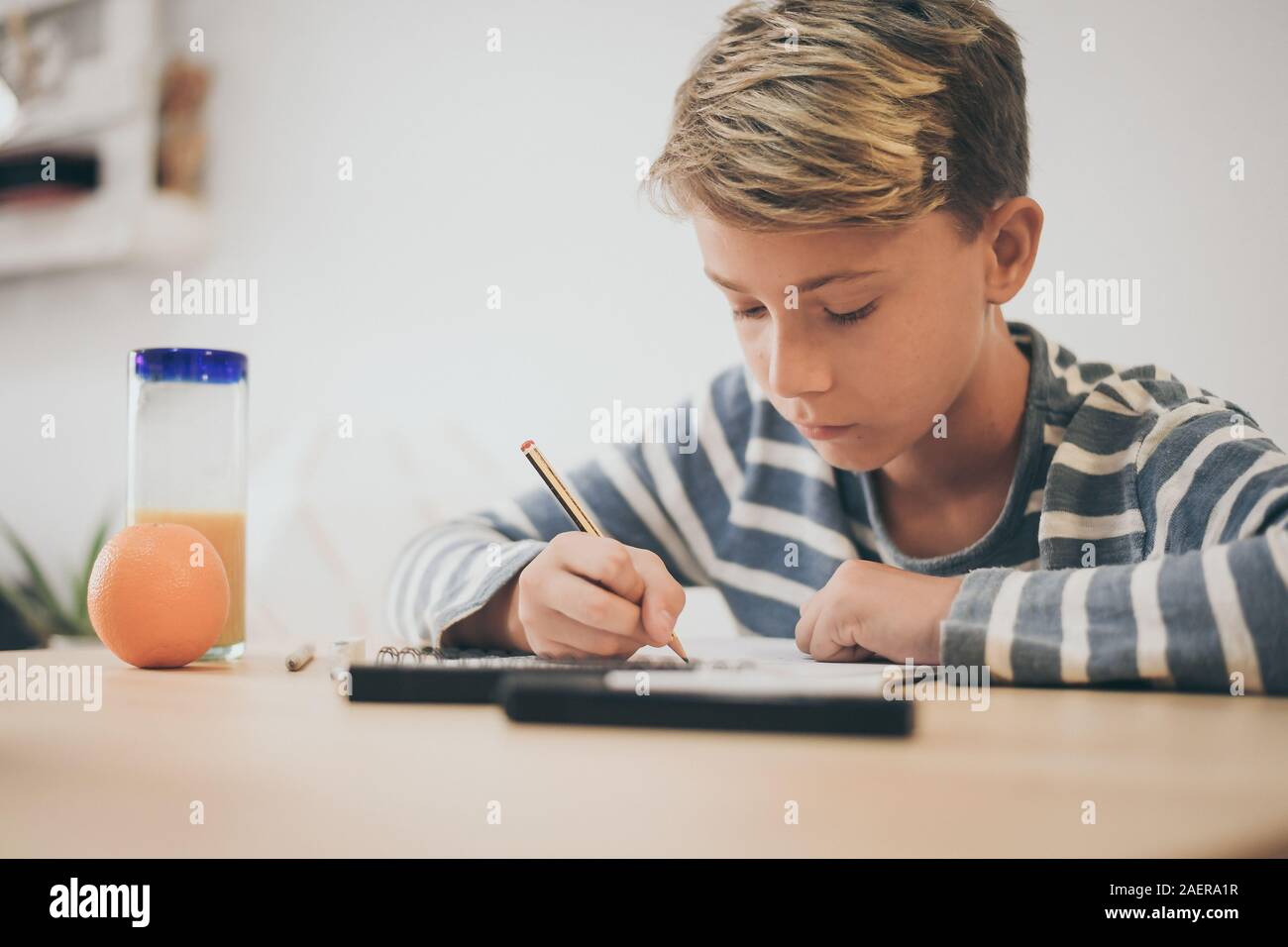 Student drawing with pencil on the notebook. Boy doing homework writing on a paper. Kid hold a pencil and draw a manga at home. Teen drawing sitting a Stock Photo