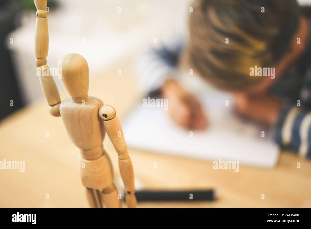 Student drawing with pencil a human figure be inspired by a wooden model.  Boy copying a dummy for school art tasks. Kid hold a pencil and draw a  manga Stock Photo 