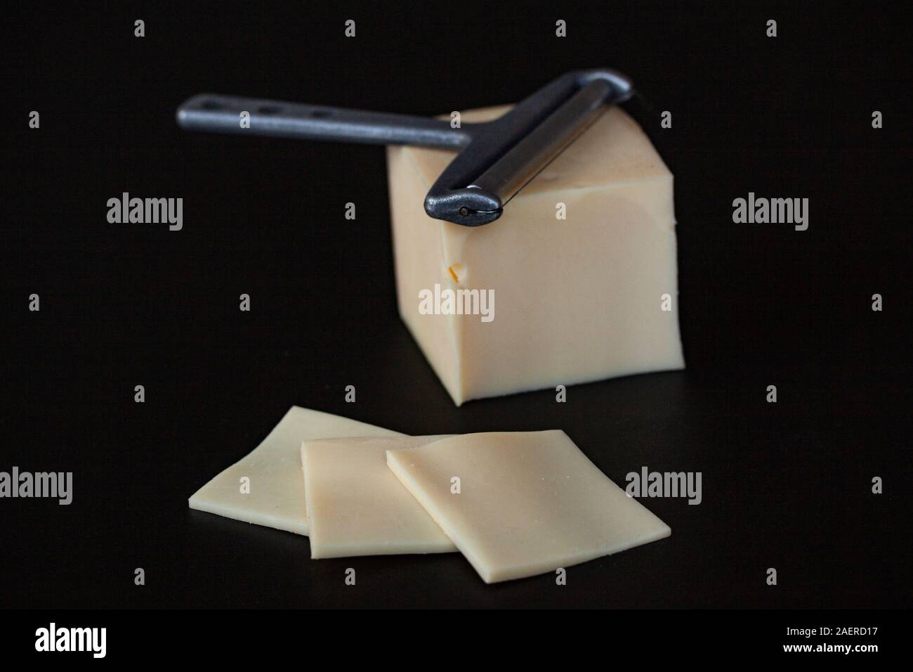 https://c8.alamy.com/comp/2AERD17/slices-of-yellow-cheese-and-a-cheese-slicer-lying-on-a-block-of-cheese-on-black-background-selective-focus-close-up-image-2AERD17.jpg