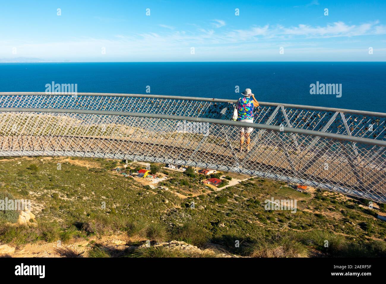 Middle aged woman wearing a sun hat looking at the view from the Santa Pola Skywalk viewing platform on the cliffs above Partida Bancal de la Arena, A Stock Photo