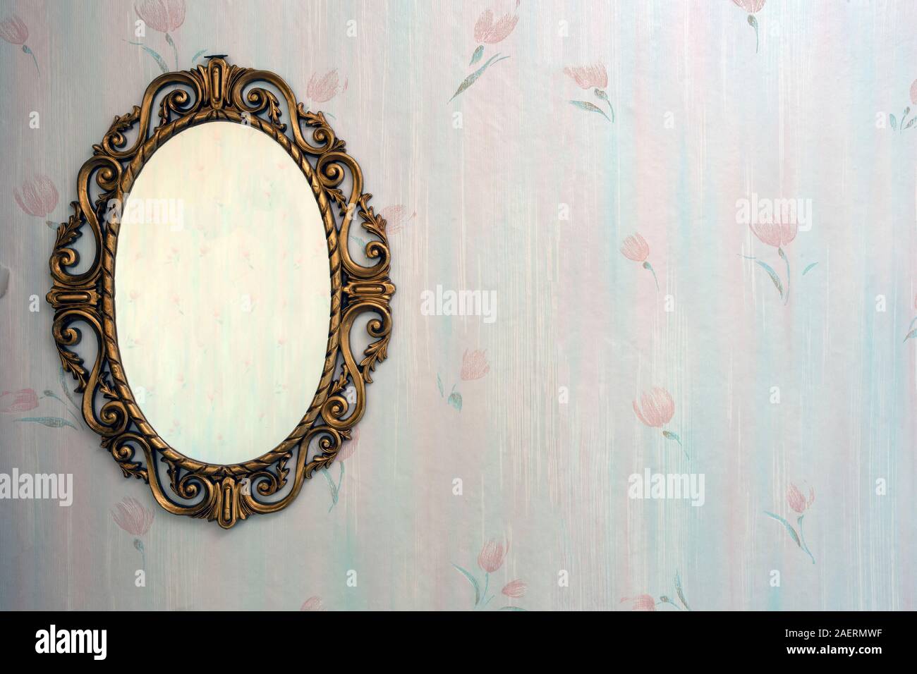 Old antique gold mirror hanging in a vintage room with old pattern wallpaper Stock Photo