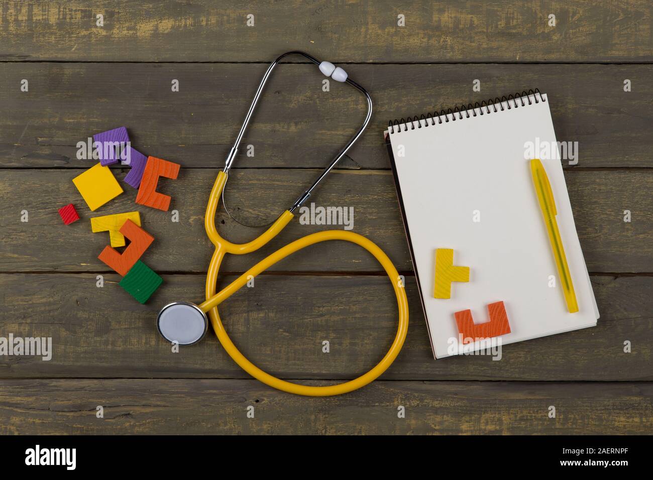 Children's healthy development concept - blank notepad, yellow stethoscope, colorful wooden jigsaw puzzles on wooden background Stock Photo