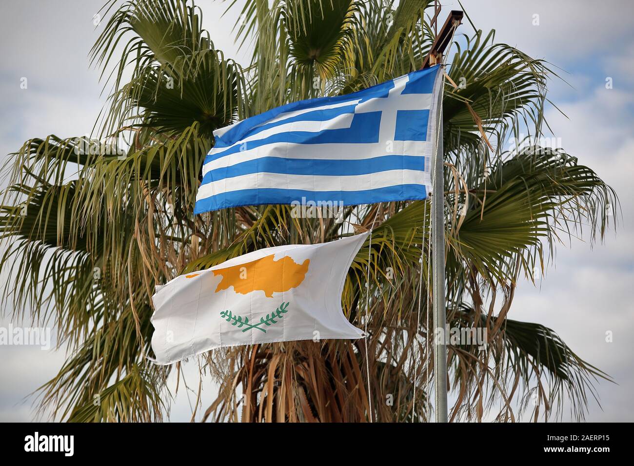 Flags of Greece and Cyprus on flagpole wave on wind together against green palm tree. Stock Photo