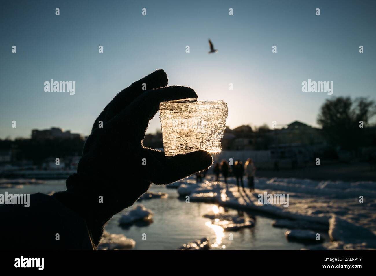 Woman's hand in a black glove holding a broken piece of sea ice against the sun. Person looking through the ice at the sun Stock Photo
