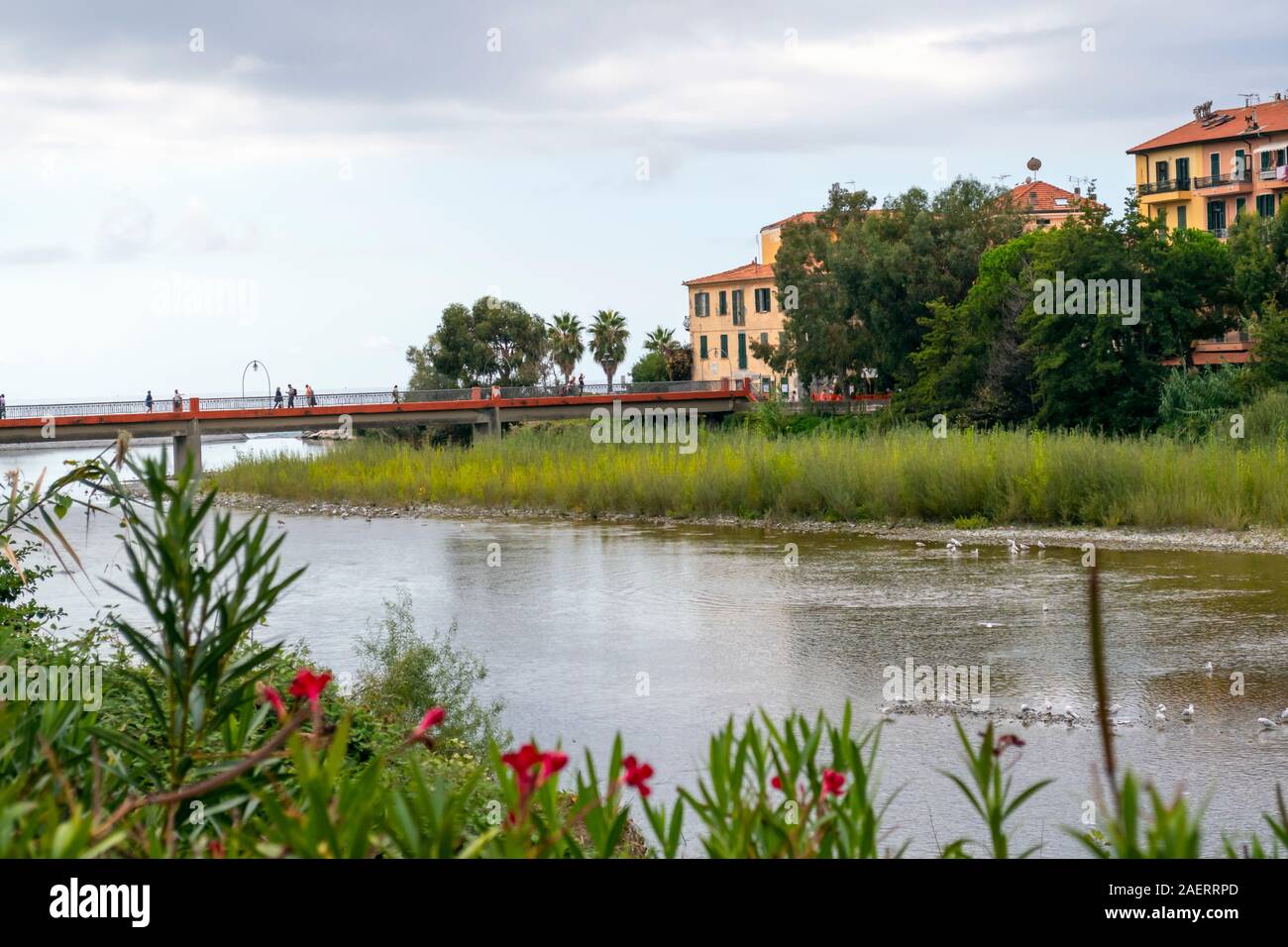 Tourists cross the bridge over the river Roia separating the two sections of Ventimiglia on the Italian Riviera. Stock Photo