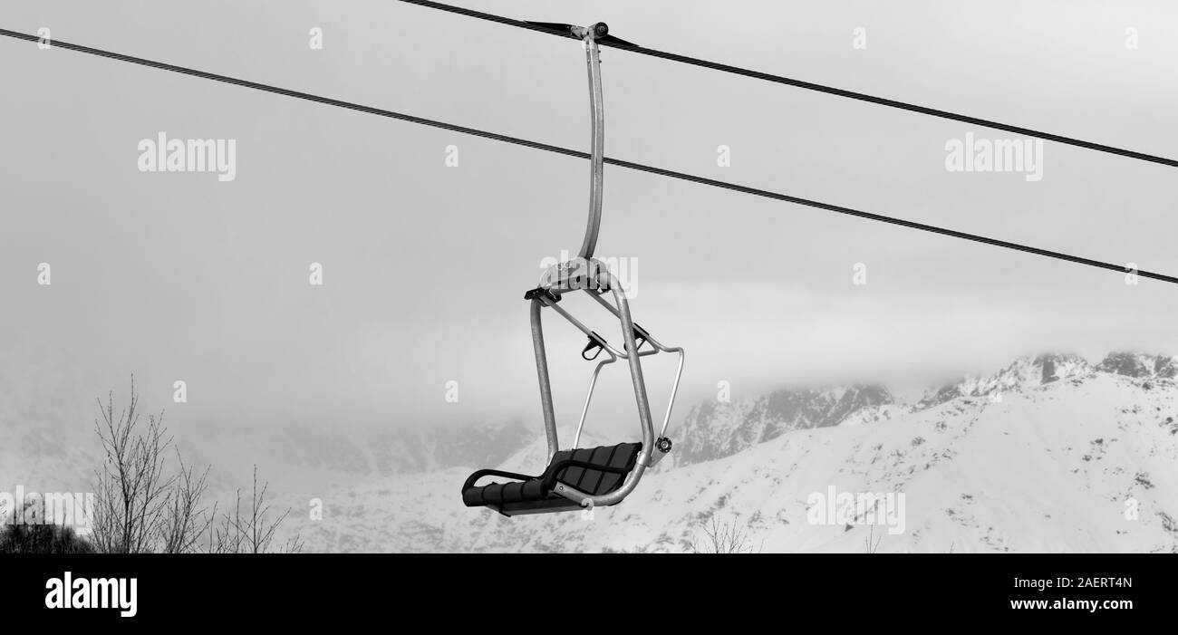 Chair lift and snowy mountains in haze at winter. Caucasus Mountains. Hatsvali, Svaneti region of Georgia. Black and white toned landscape. Panoramic Stock Photo