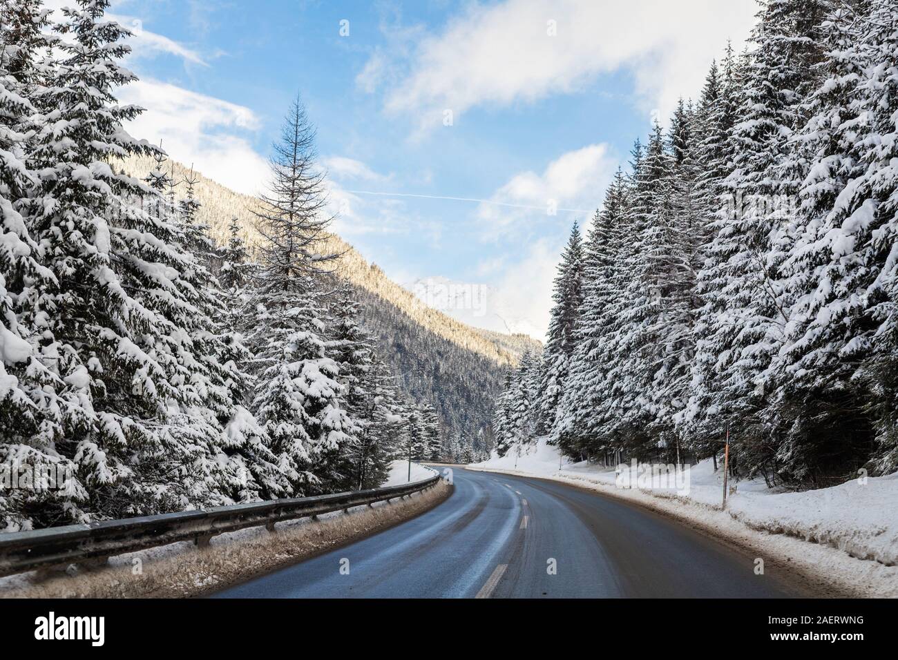 Winter alpine road curve landscape with forest, mountains and blue sky on background at bright cold sunny day. Car trip family travel journey. Holiday Stock Photo
