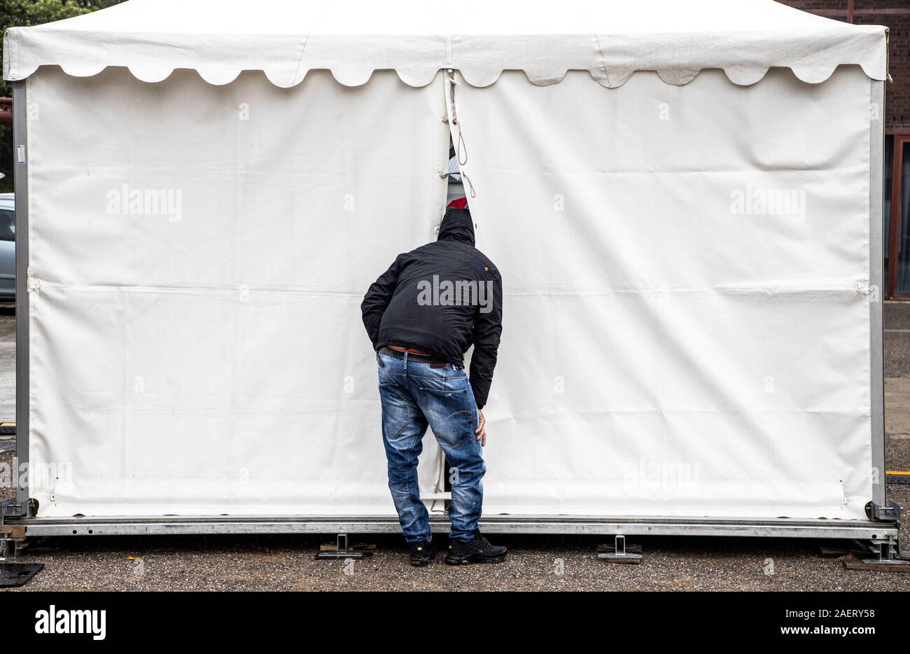 Curiosity, curious man, puts his head into an event tent, through a crack and watches from outside, Stock Photo
