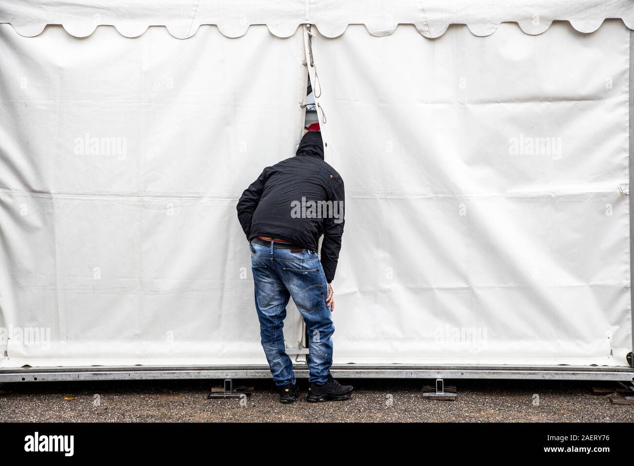 Curiosity, curious man, puts his head into an event tent, through a crack and watches from outside, Stock Photo