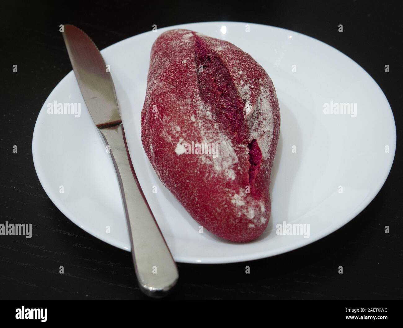 Red beet bread bun with a knife on a white plate Stock Photo