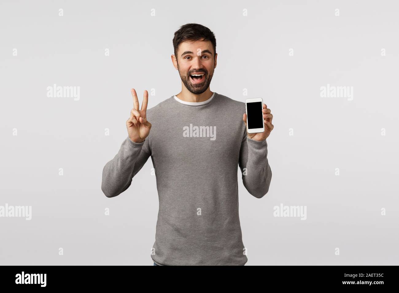 Friendly and carefree funny bearded gay man in grey sweater edit profile  picture online dating app, make peace sign, showing smartphone display and  Stock Photo - Alamy
