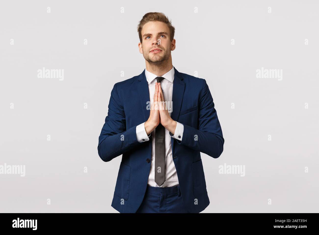 Hopeful attractive blond caucasian guy, male entrepreneur in classic suit, business formal wear, hold hands together in pray, look up sky like Stock Photo