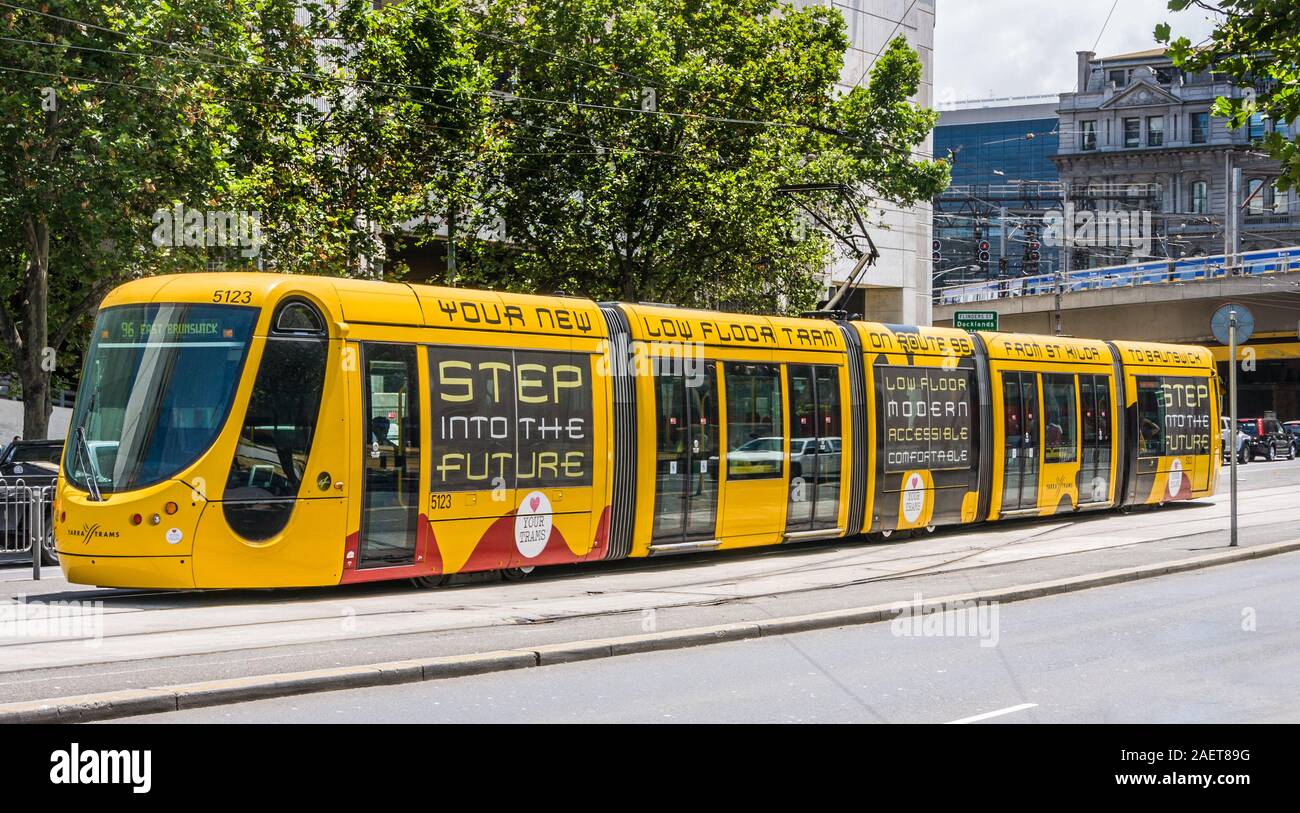 Melbourne, Australia - November 16, 2009: Closeup of modern new yellow Low Floor Tram on its tracks in light gray street with green foliage above. Ste Stock Photo