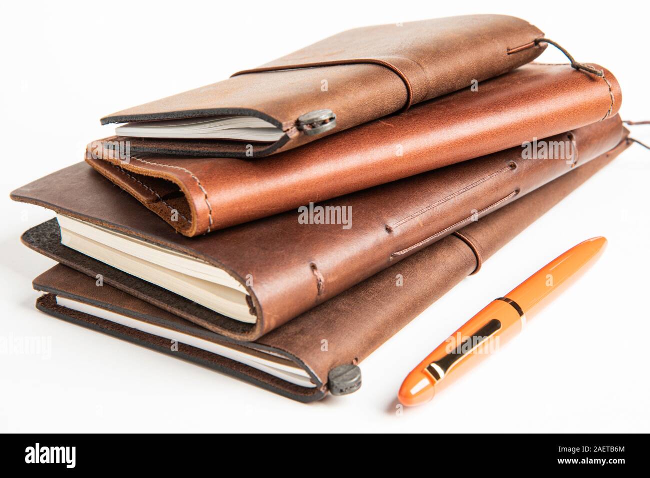 A stack of leather-bound travel writing journals with an orange fountain pen set on plain white background, Stock Photo