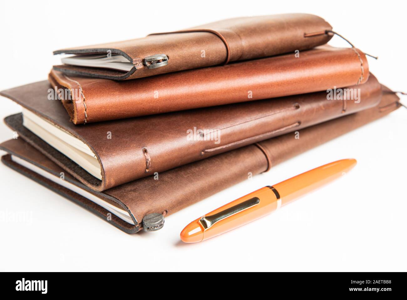 A stack of leatherbound travel writing journals with an orange fountain pen set on plain white