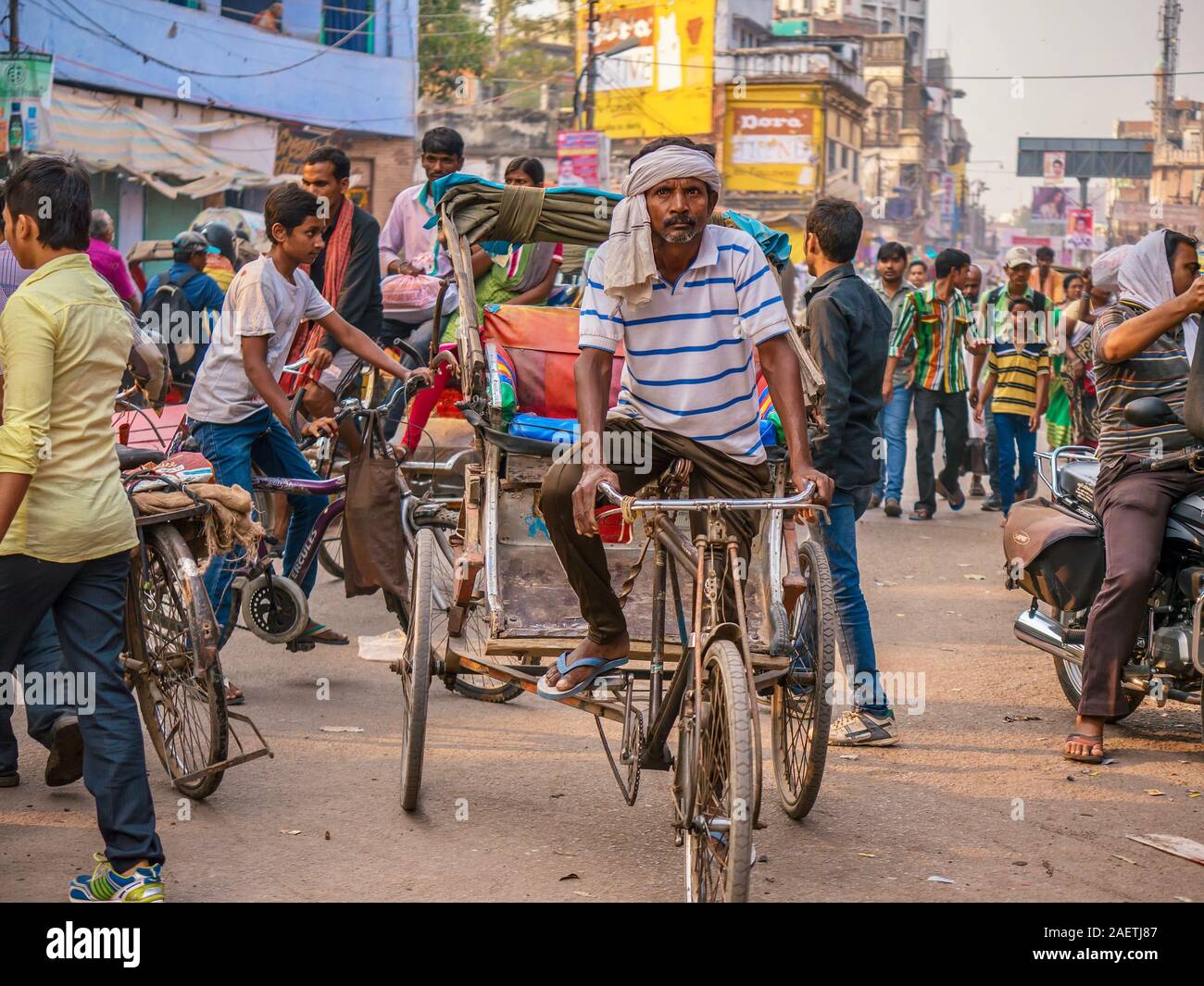 a male rickshaw driver pedaling his dilapidated cab through a busy street crowded with other drivers and pedestrians in northern India. Stock Photo