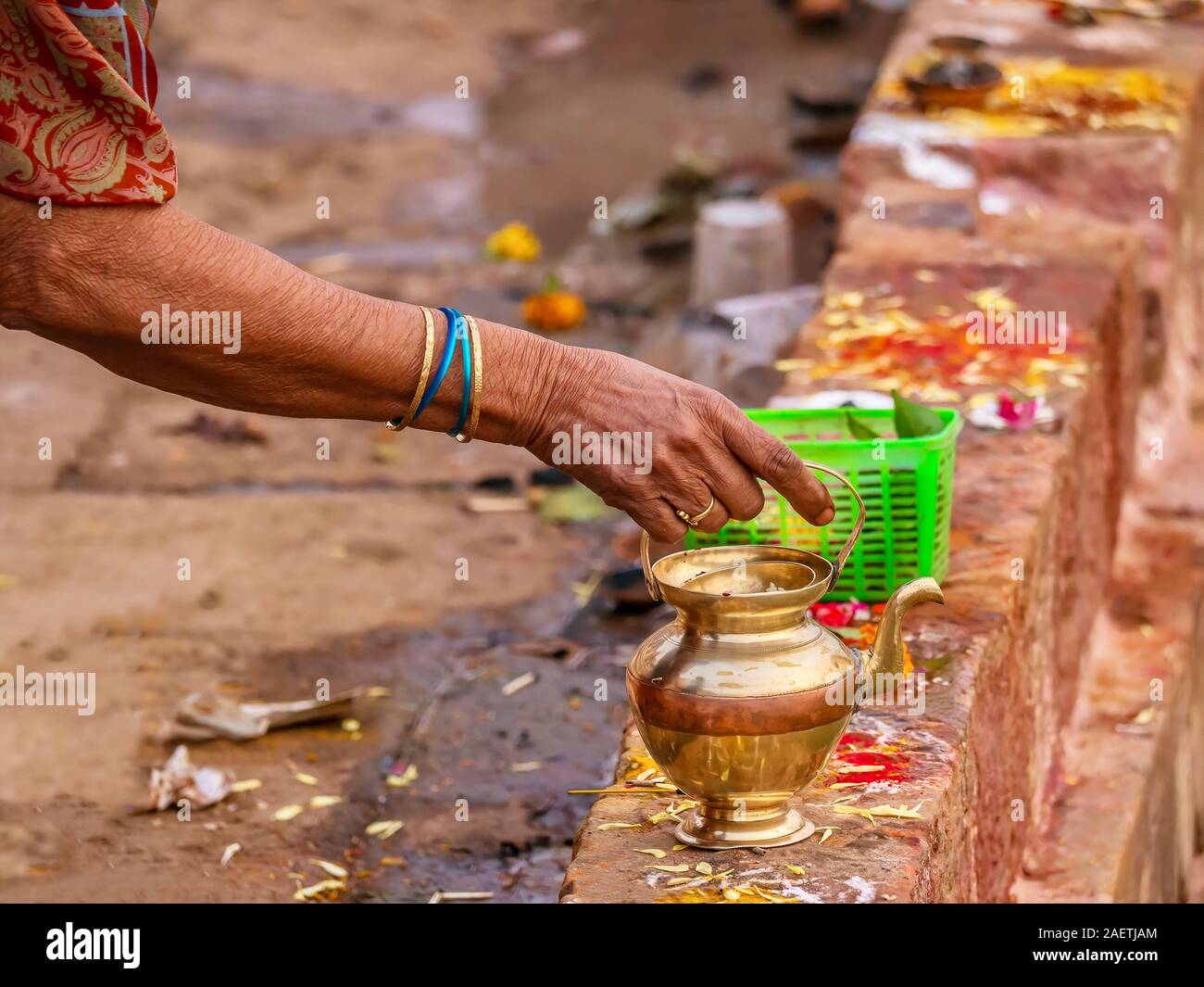 A woman prepares a personal offering to a Hindu deity using a brass pot, a basket of betel leaves and fruit, and colorful kumkum powder. Stock Photo