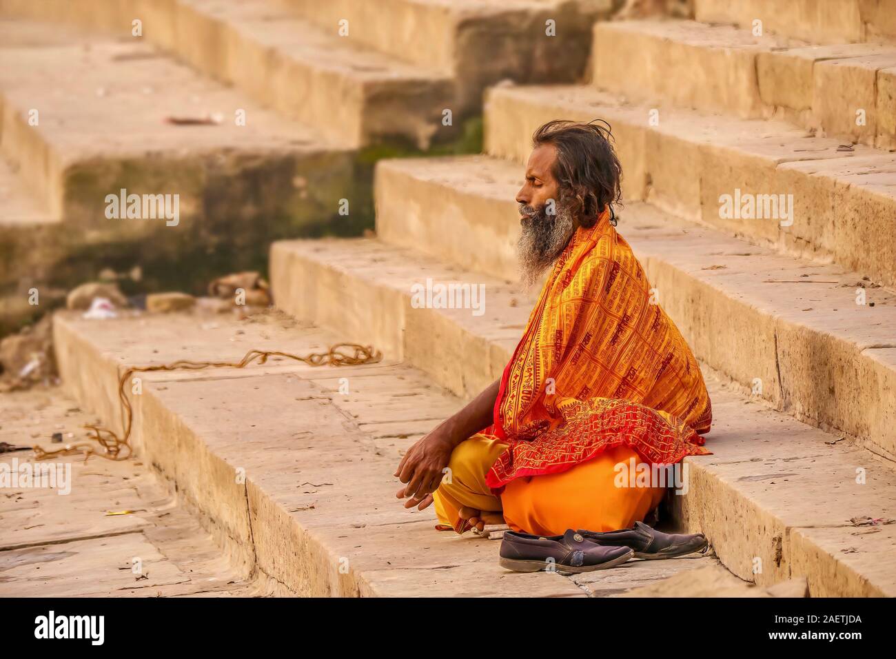 An Indian sadhu sits cross-legged in meditation on the public ghats of the ancient city of Varanasi at dawn. Stock Photo