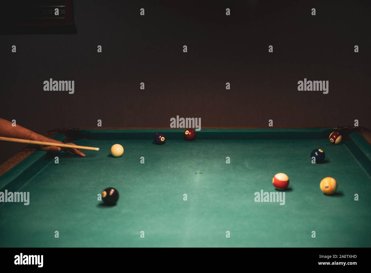 Male lines up billiard shot to sink a ball by the corner pocket Stock