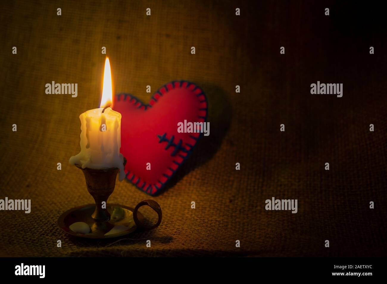 Burning candle on a vintage candlestick and a small red stitched fixed broken  heart in the dark against sack cloth background with copy space. Magical  Stock Photo - Alamy, image size:1300x955