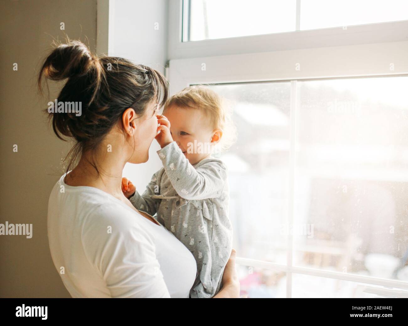 Young woman mom with baby girl on hands near window at the home Stock Photo