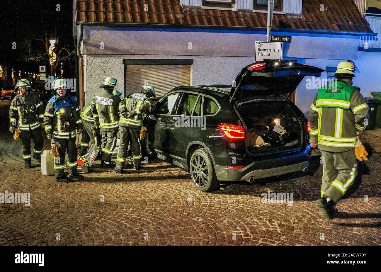 Gerlingen, Germany. 11th Dec, 2019. Firefighters are standing next to a car  with a destroyed hood in front of a partially smashed living room wall of a  detached house. A 26-year-old female