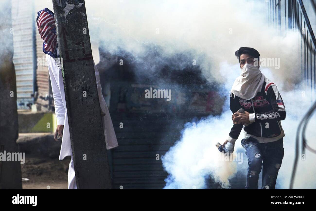 A Kashmiri Muslim protester prepares to throw back a tear gas canister at Indian security personnel as another takes cover behind an electric pole Stock Photo