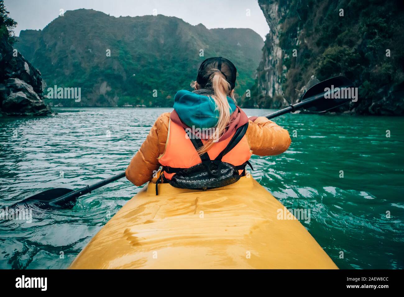 Girl kayaking on the seaside of Halong bay in Vietnam. Woman rowing oars in the boat. The view from the back. Stock Photo