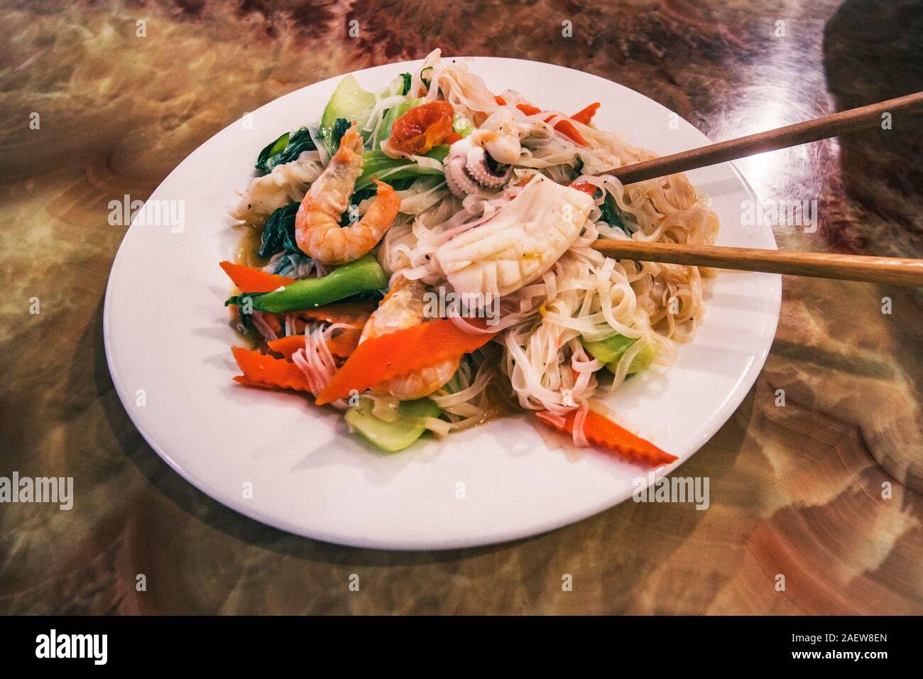Seafood pad Thai dish of Thai fried rice noodles on a white plate with chopsticks and grated carrot garnish. Stock Photo