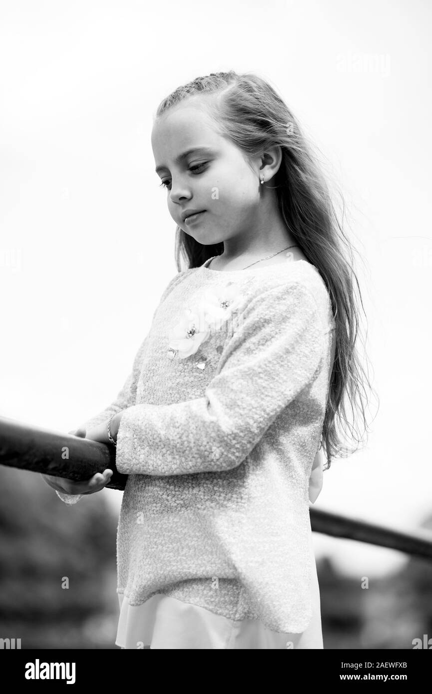 Small girl in trendy clothes on natural background. Child with long blond hair outdoor. Kid model in fashionable dress. Fashion style and trend. Lost in thoughts. Childhood and childcare. Stock Photo