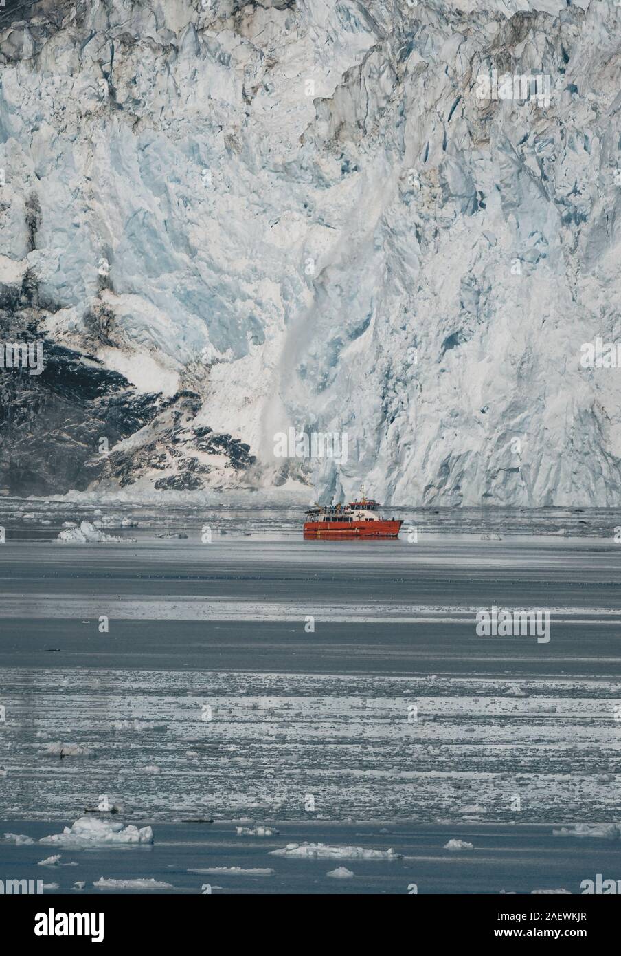 Red Passenger cruise ship sailing through the icy waters of Qasigiannguit, Greenland with Eqip Sermia Eqi Glacier in Background. Ice breaking off from Stock Photo