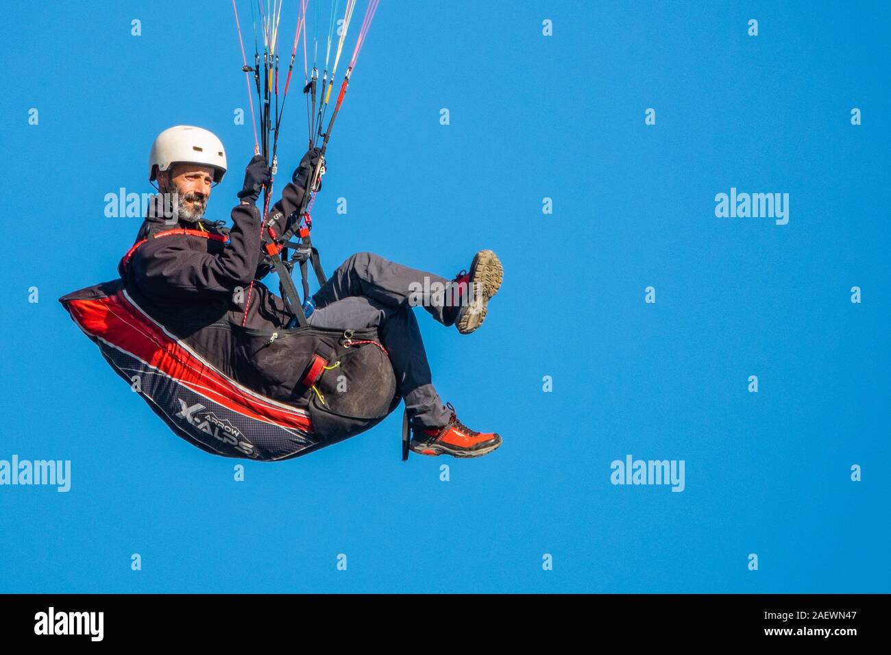 Bearded man seated in a paragliding rig in flight, full frame blue sky background, copy space Stock Photo