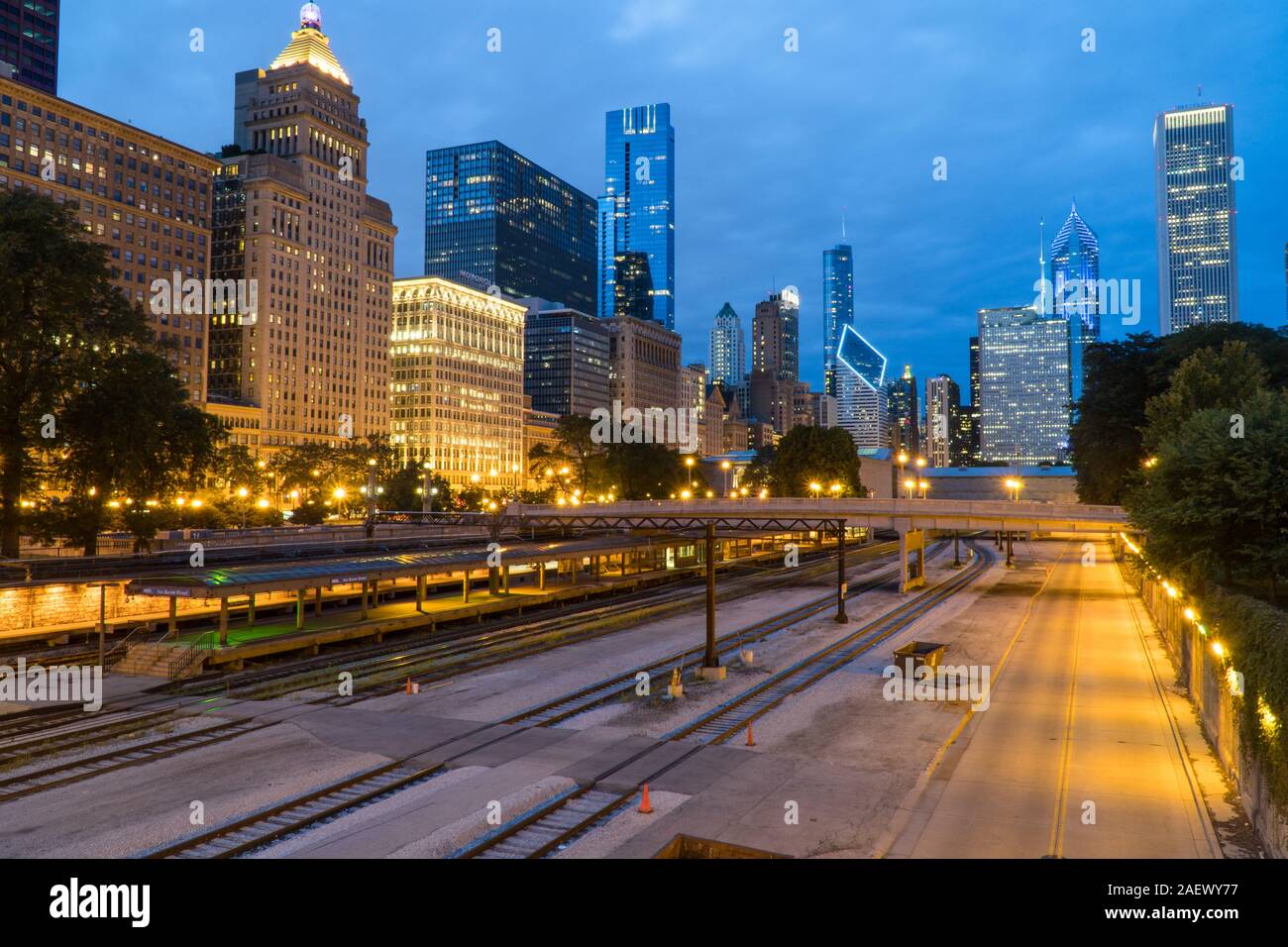 Evening twilight exterior skyline shot of downtown Chicago at night with building cityscape illuminating the dark sky view over train track rail yard Stock Photo