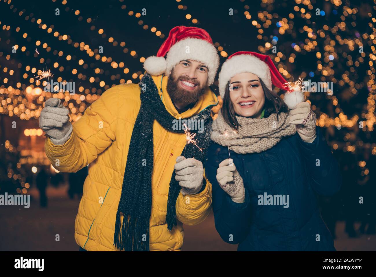 Photo of couple guy lady two people at x-mas celebration in park holding magic sparklers at outdoors newyear party wearing warm coats santa caps Stock Photo