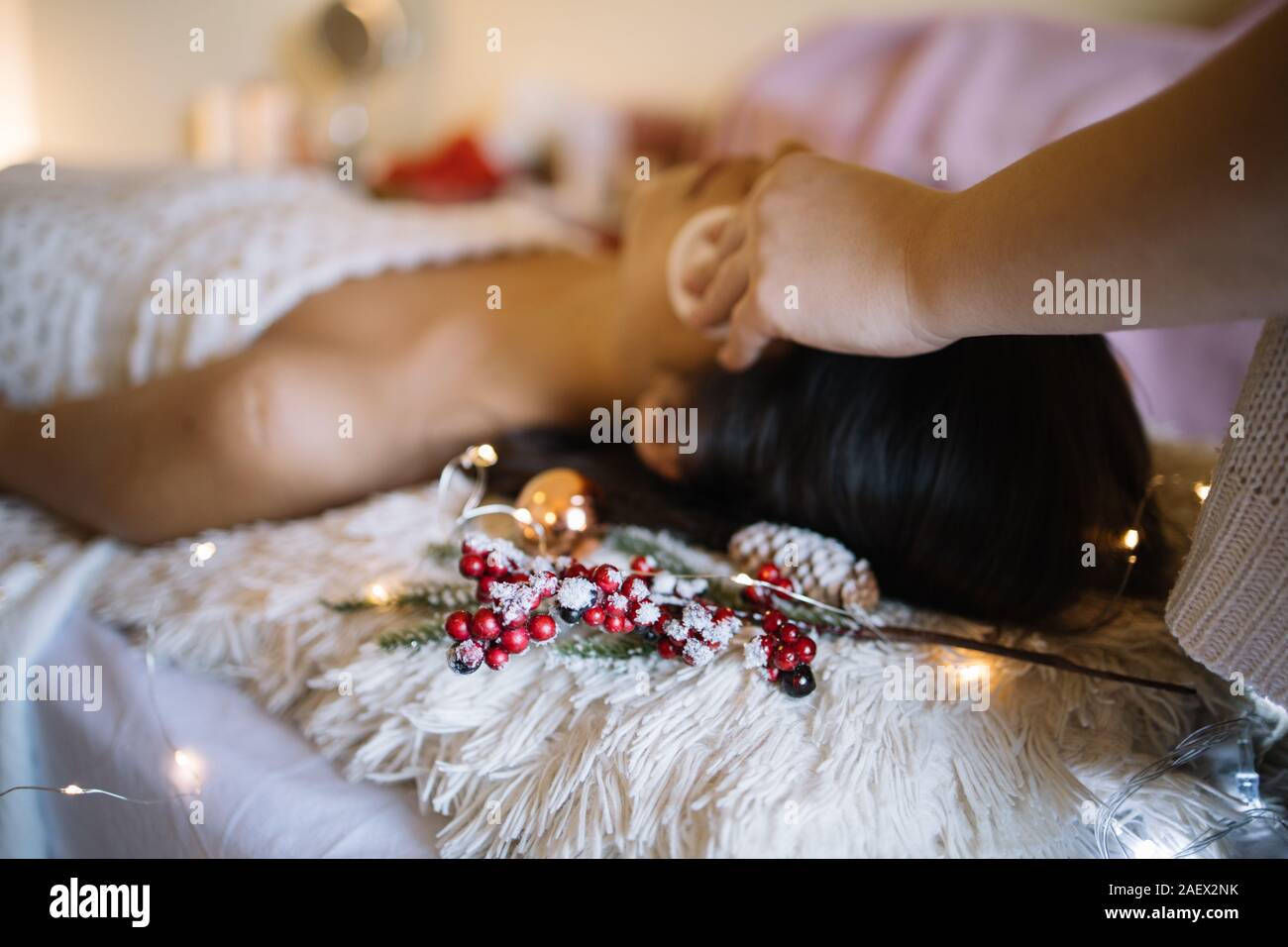 Pine Twig With Red Berries And Lights At Spa Center Christmas Lights With Pine Twig And Ball Next To Out Of Focus Woman Lying On Bed At Beauty Salon Stock Photo