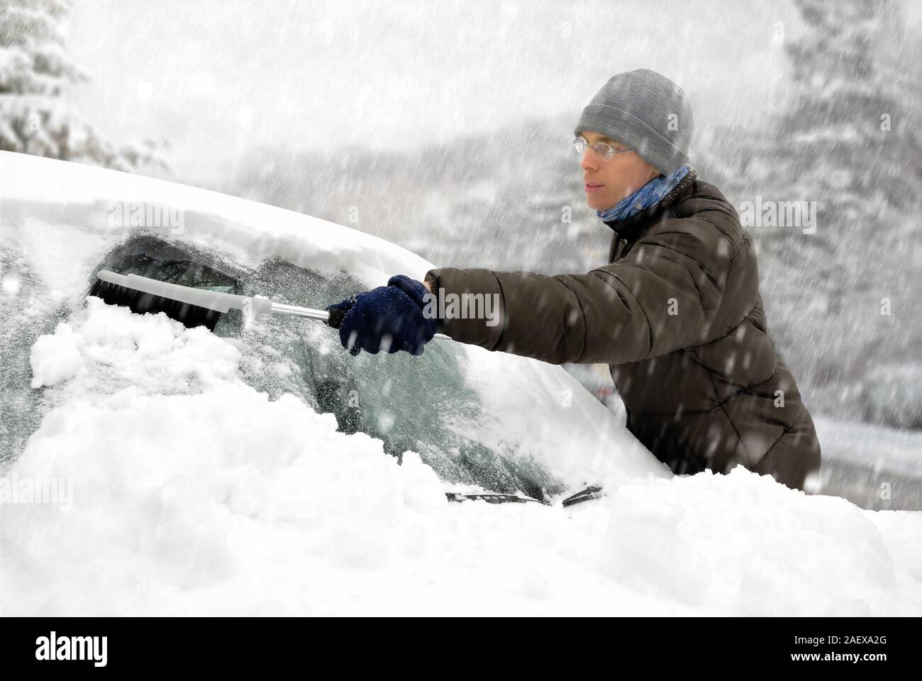 Young man brushing the snow off his car on a cold winter day in snowfall Stock Photo