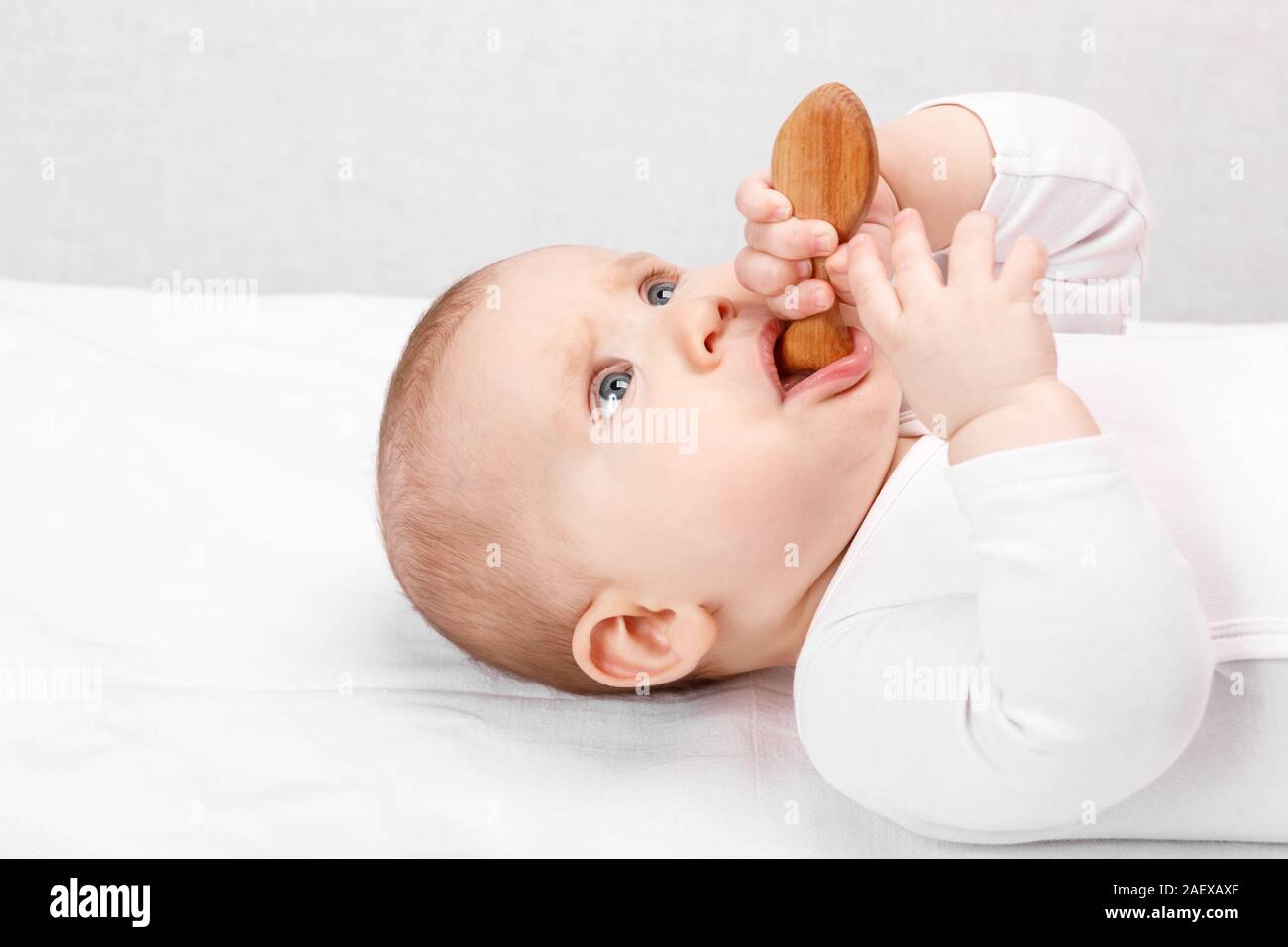 Six month baby girl chewing wooden teething toy lying on her back Stock Photo