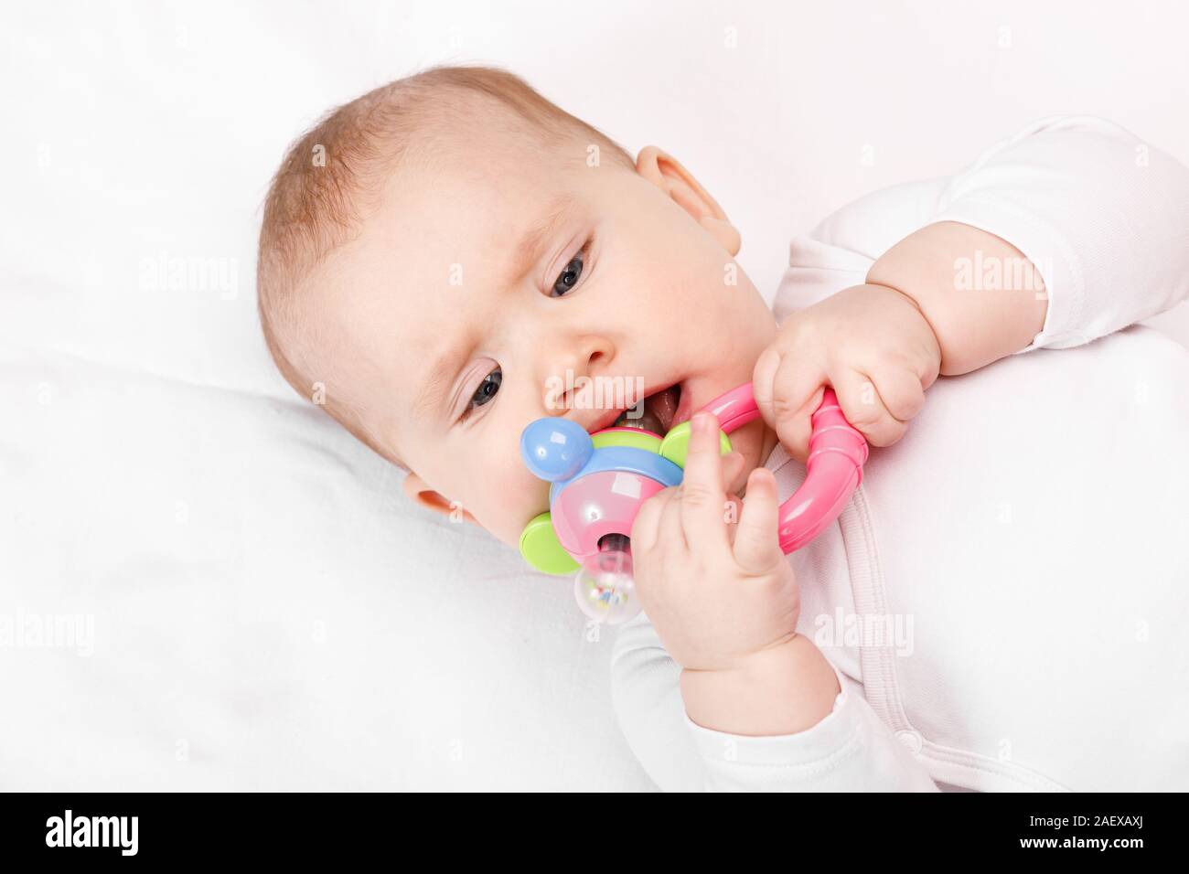Six month baby girl chewing plastic teething toy lying on her back Stock Photo