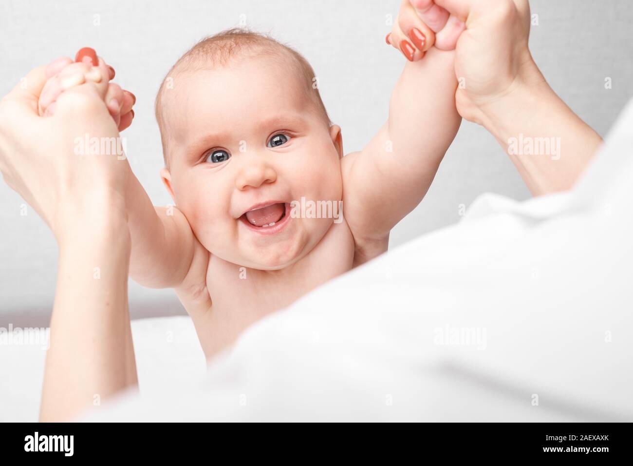 Happy six month baby girl receiving massage therapy in pediatric clinic. Manual therapist manipulates chils's arms Stock Photo