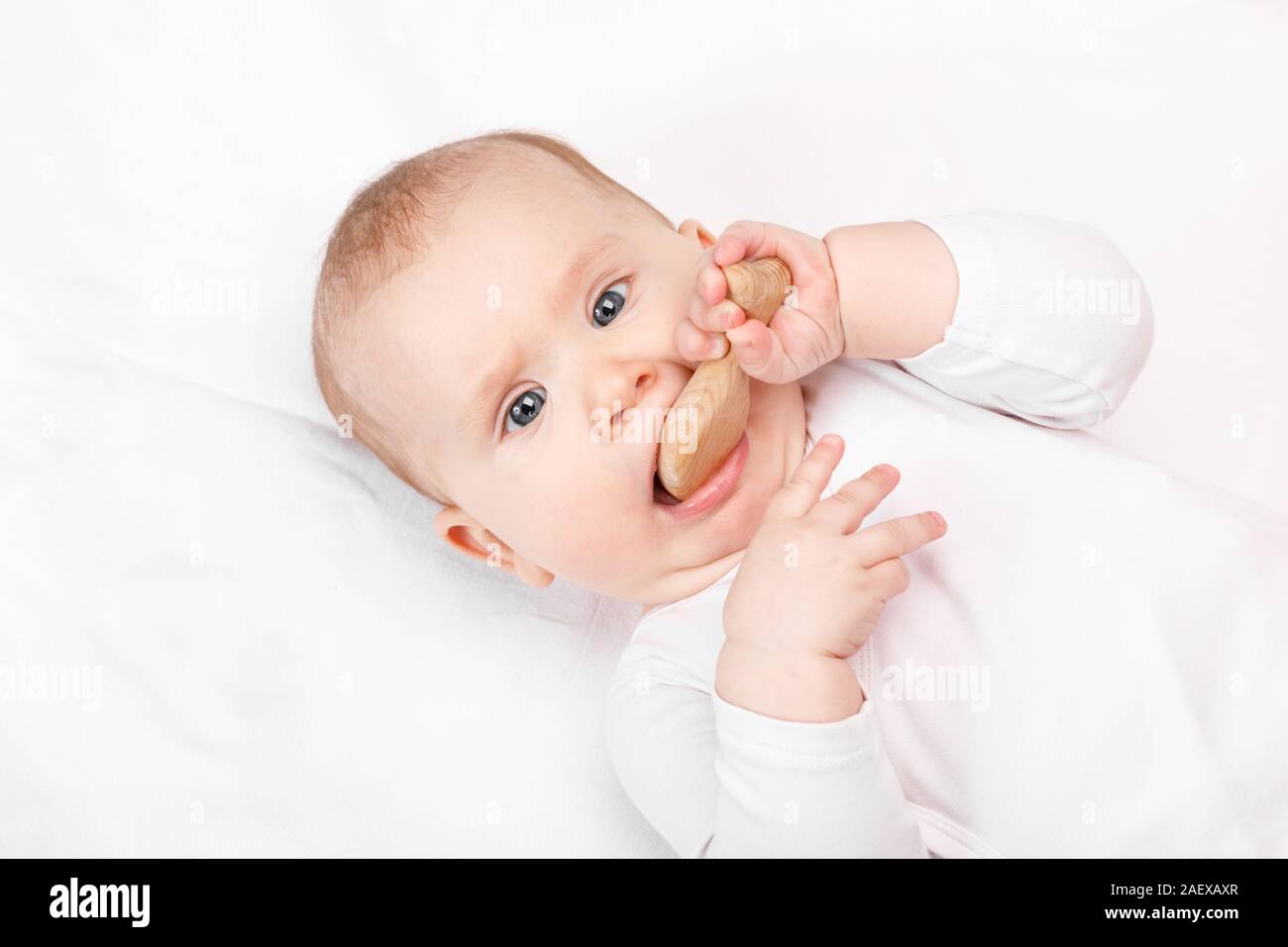 Six month baby girl chewing wooden teething toy lying on her back looking at camera Stock Photo