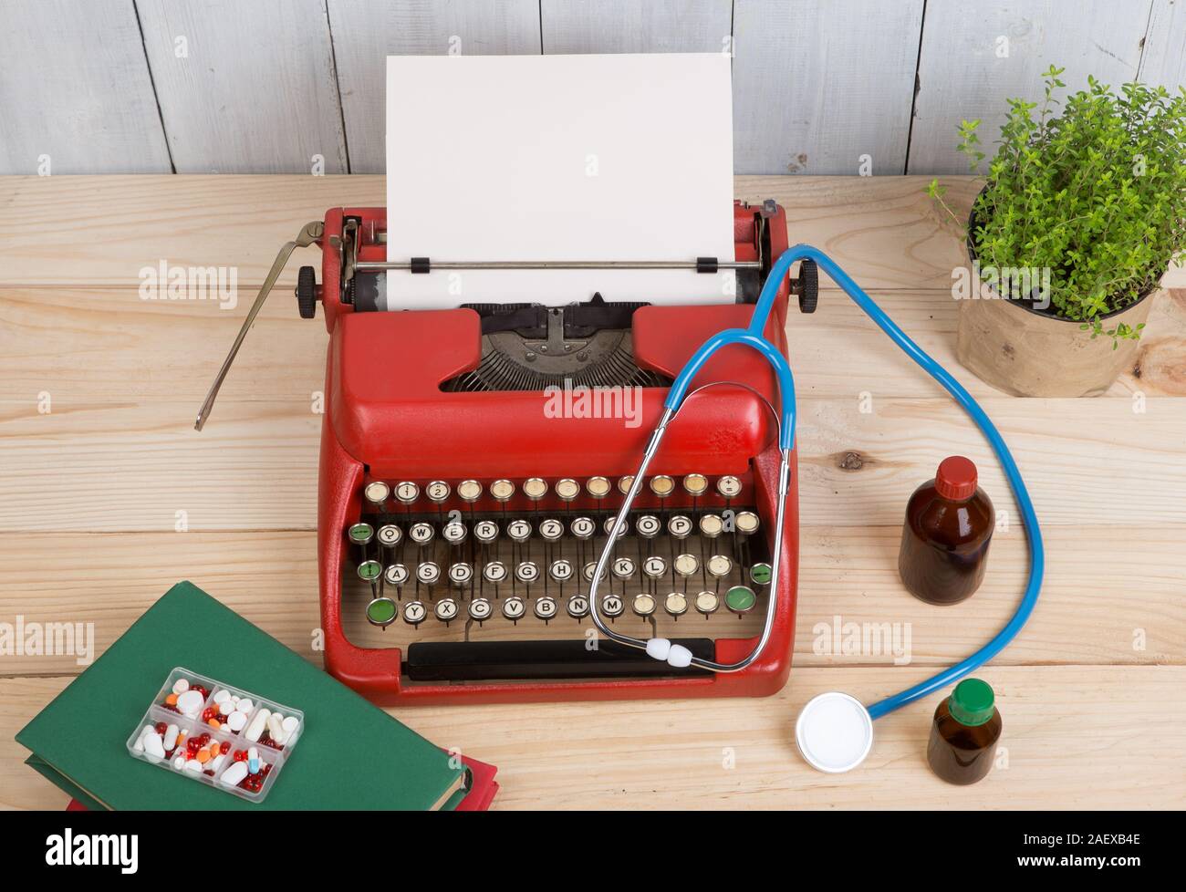 Prescription medicine or medical diagnosis - doctor workplace with blue stethoscope, pills, red typewriter with blank paper on wooden table Stock Photo