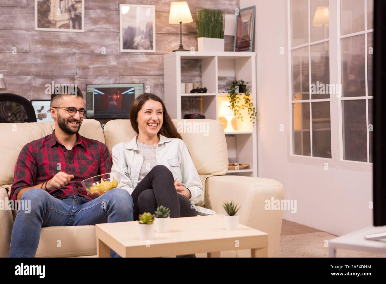 Couple laughing so hard while watching a movie on tv and eating chips